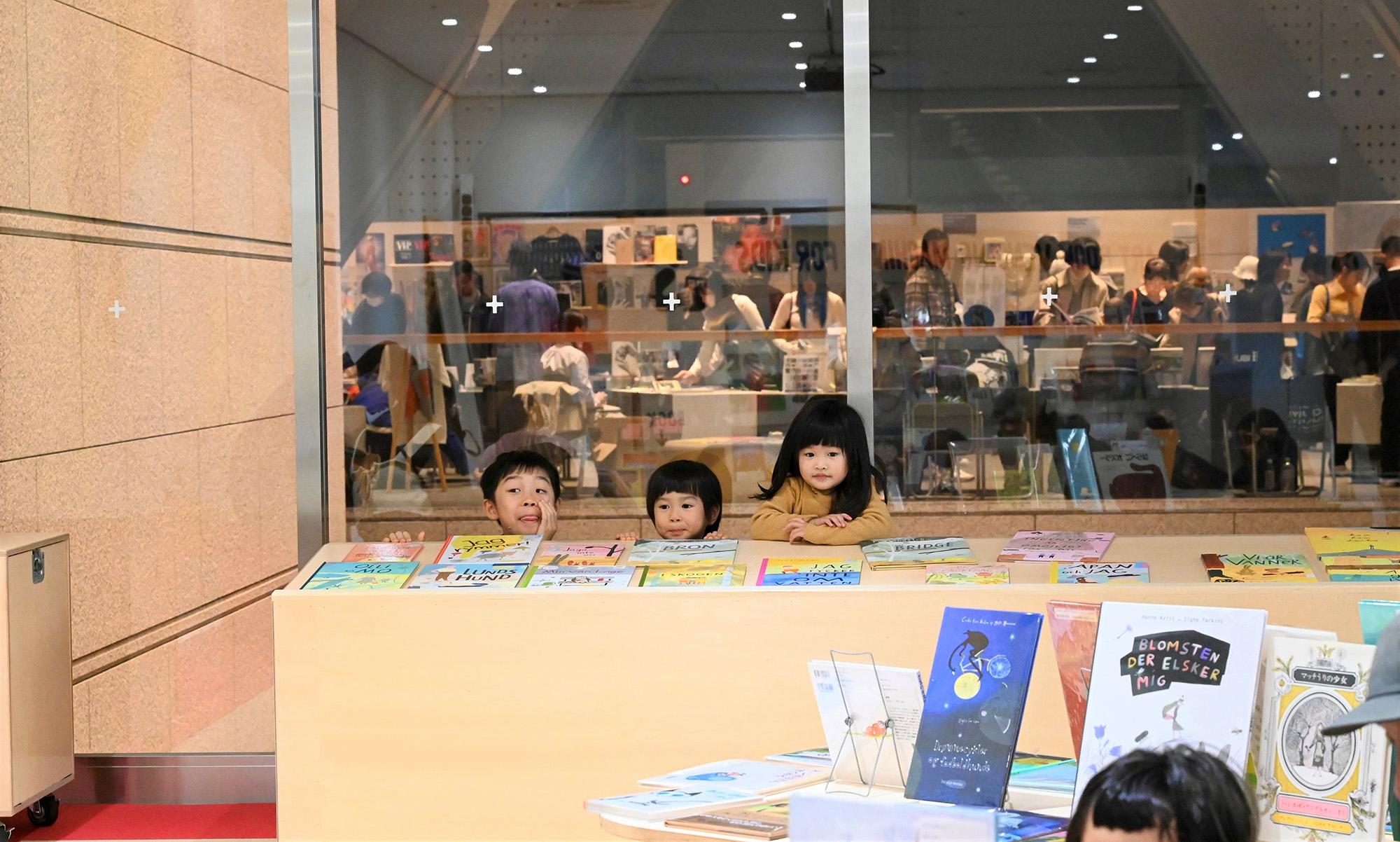 Children from Tokyo playing around bookshelves with children's books.