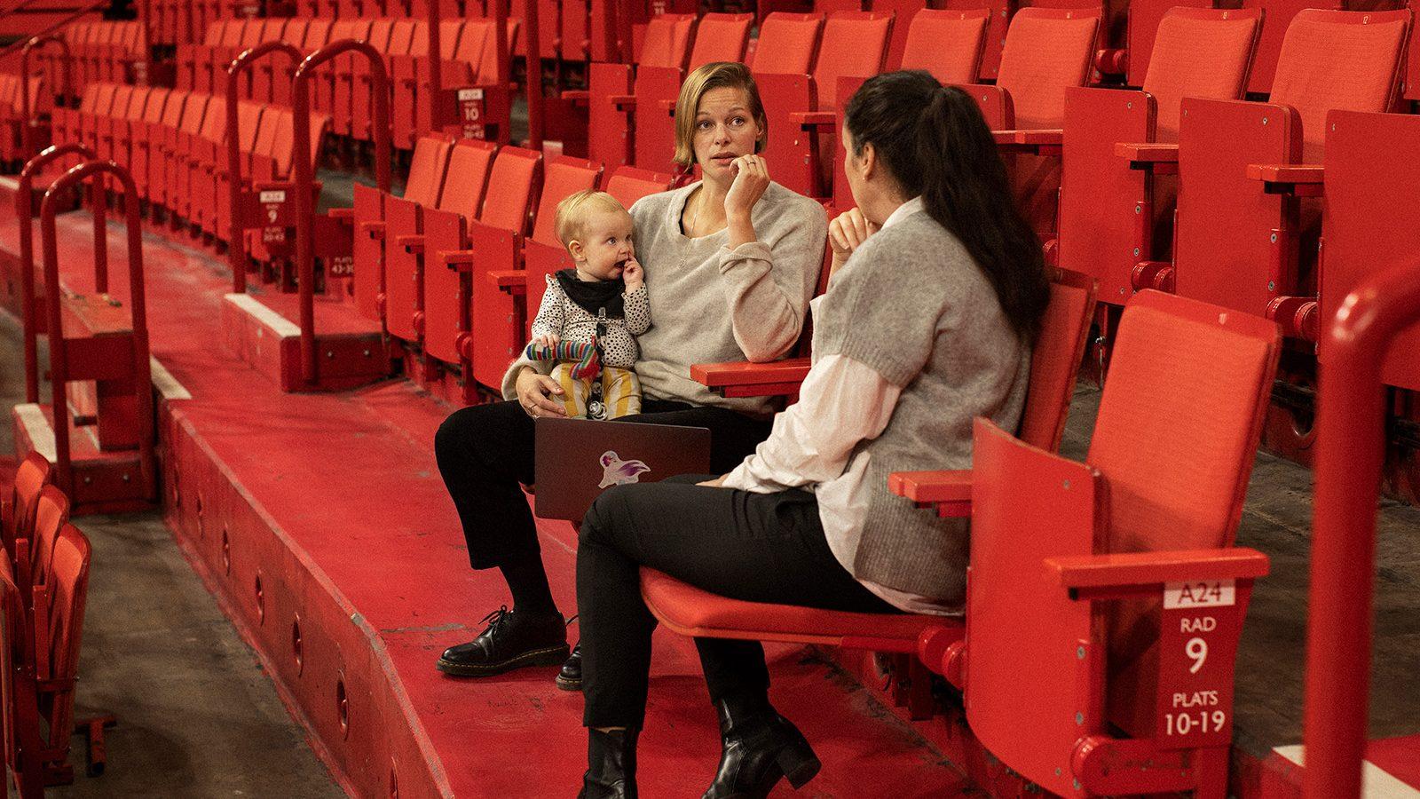 Two women having a work meeting in a theatre, one of them holding a baby.