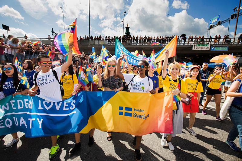 People at pride parade holding a bann and wearing t-shirts with the text 'Sweden loves equality'.