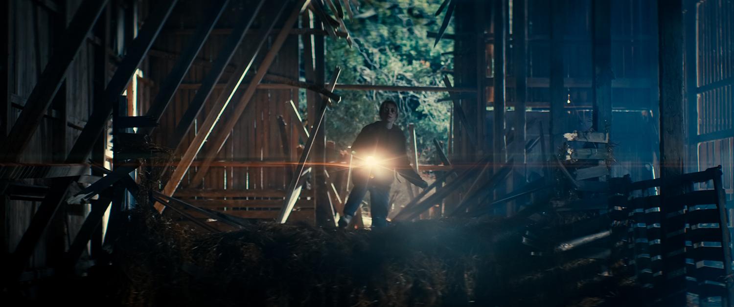 A woman with a flashlight in a dark barn.