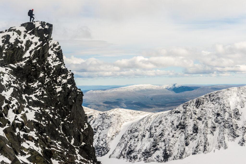 A person is on the top of a snow-covered mountain overlooking a landscape.