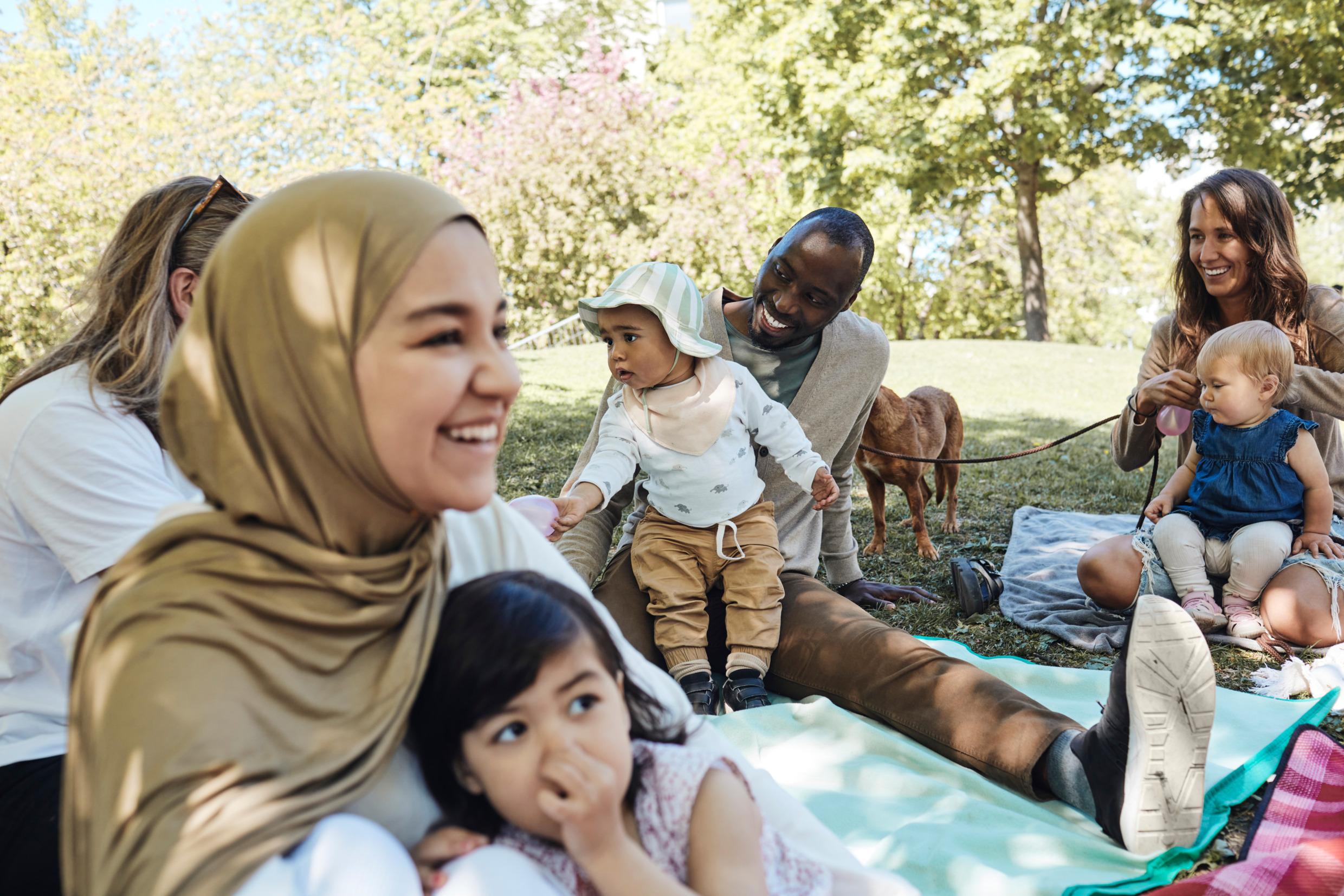 A group of adults and toddlers with different backgrounds having a picknick.