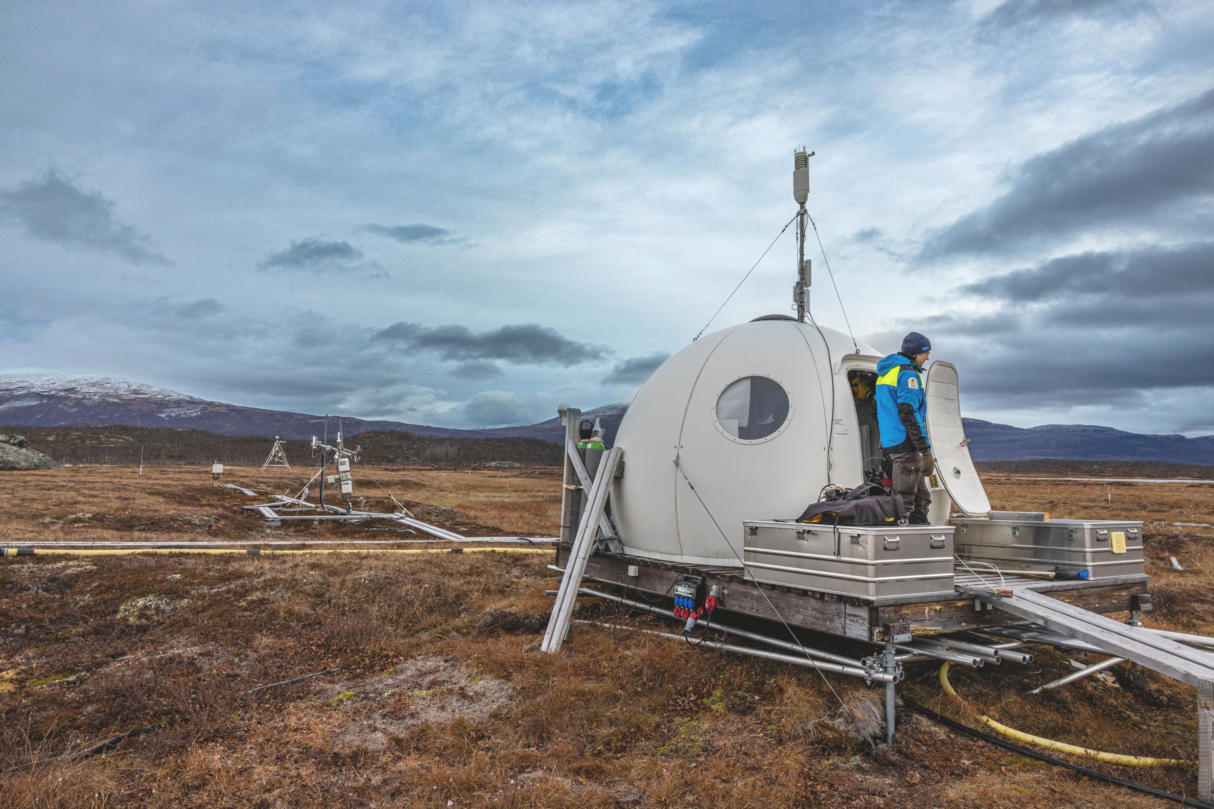 A scientist by an igloo-looking arctic research station.