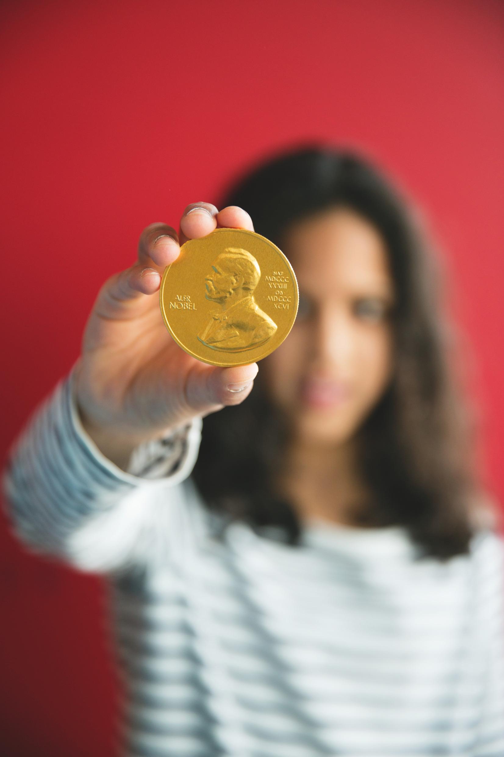 A woman holding a gold medal with Nobel's portrait.