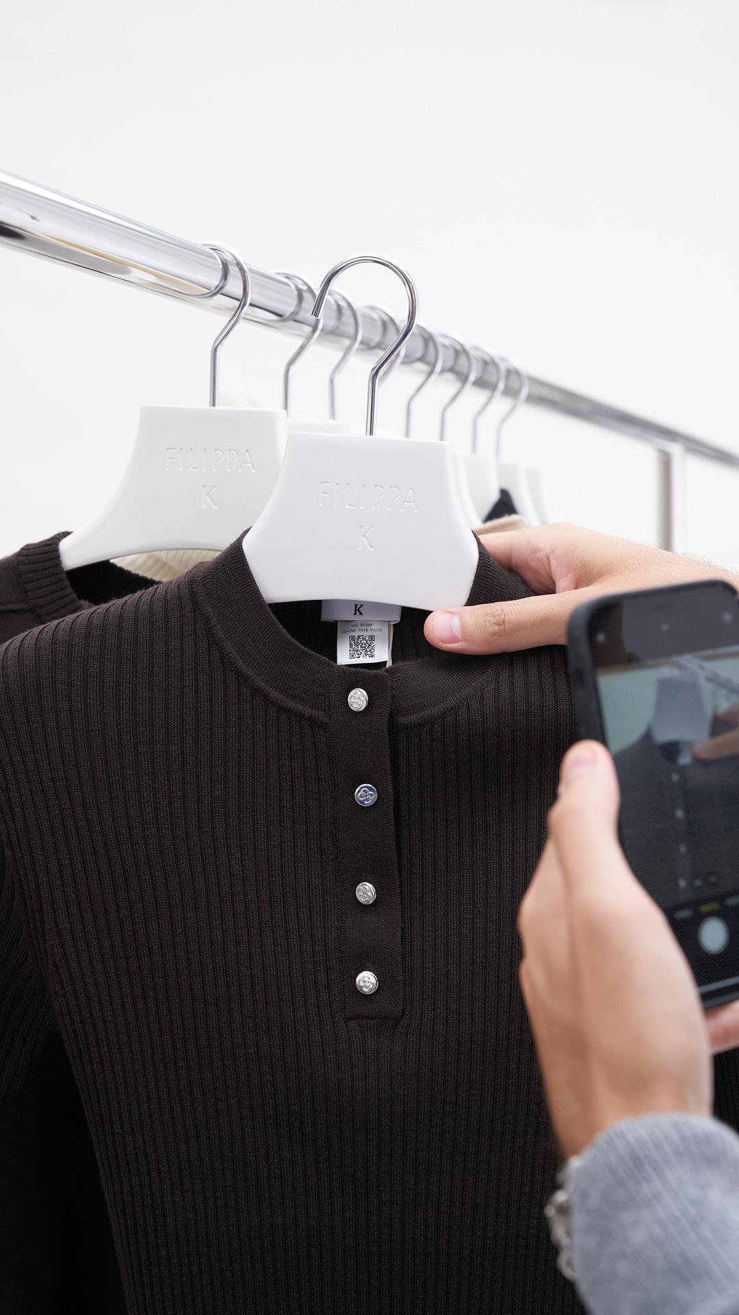 A sweater with a QR tag, on a clothing rack.