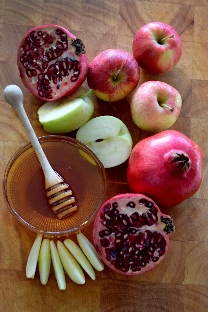 Apples, pomegranates, and honey in a bowl are arranged on a table.